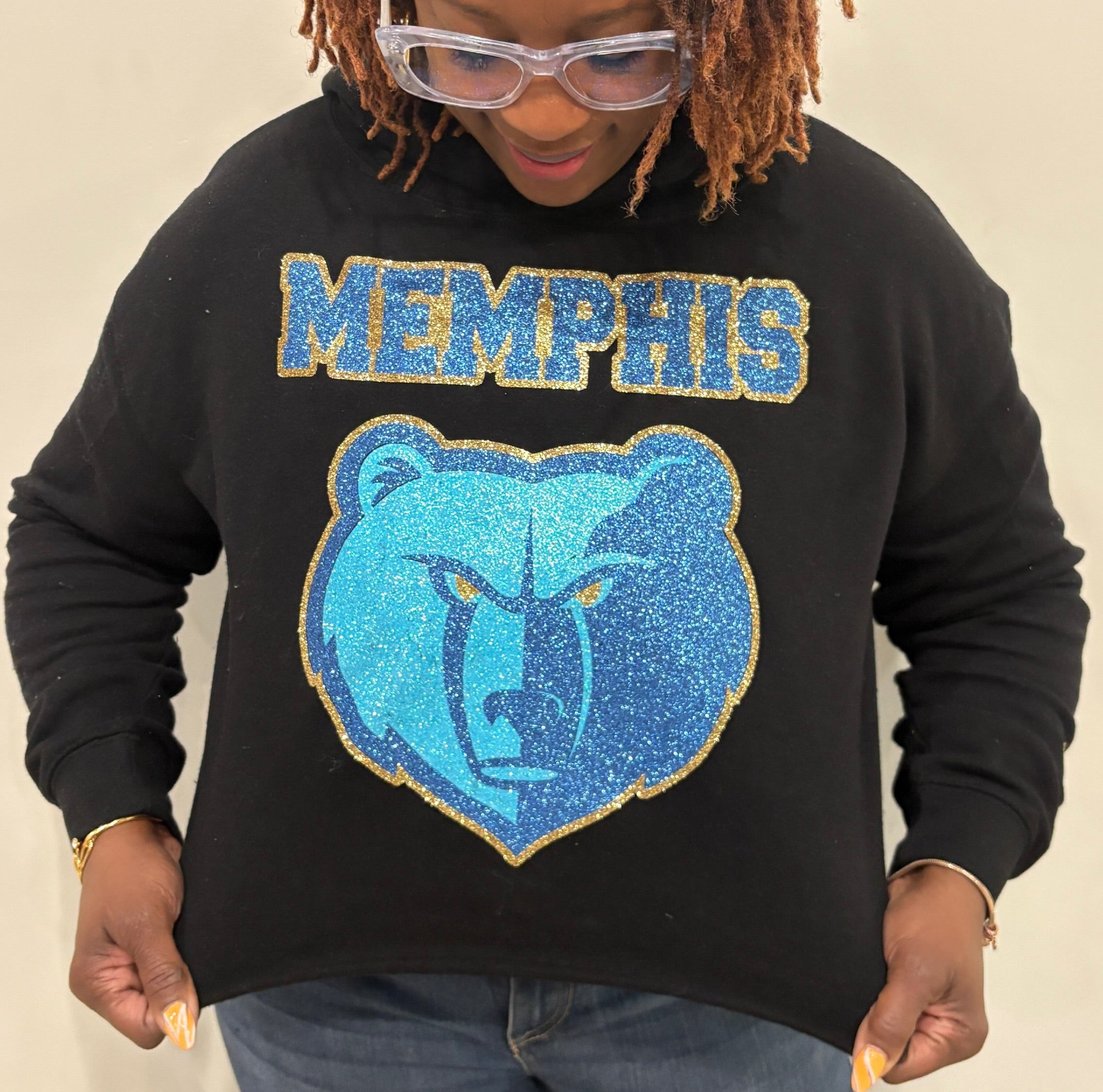 Person wearing a black sweatshirt with 'Memphis' and a bear logo on a beige background
